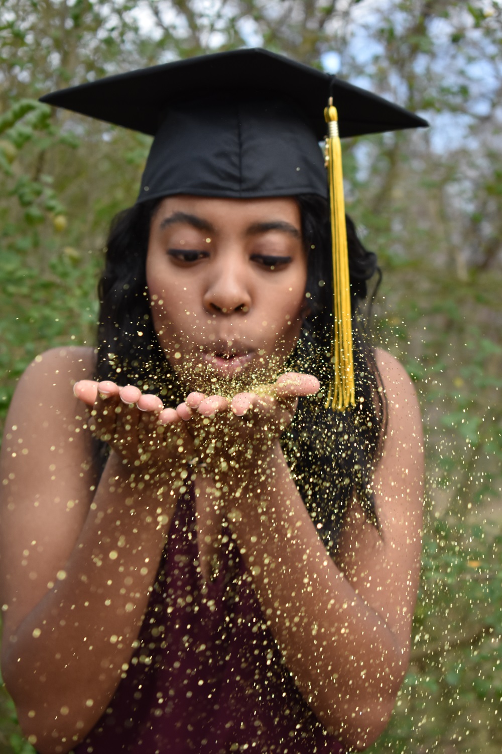 student in a graduation cap blowing gold glitter at the camera
