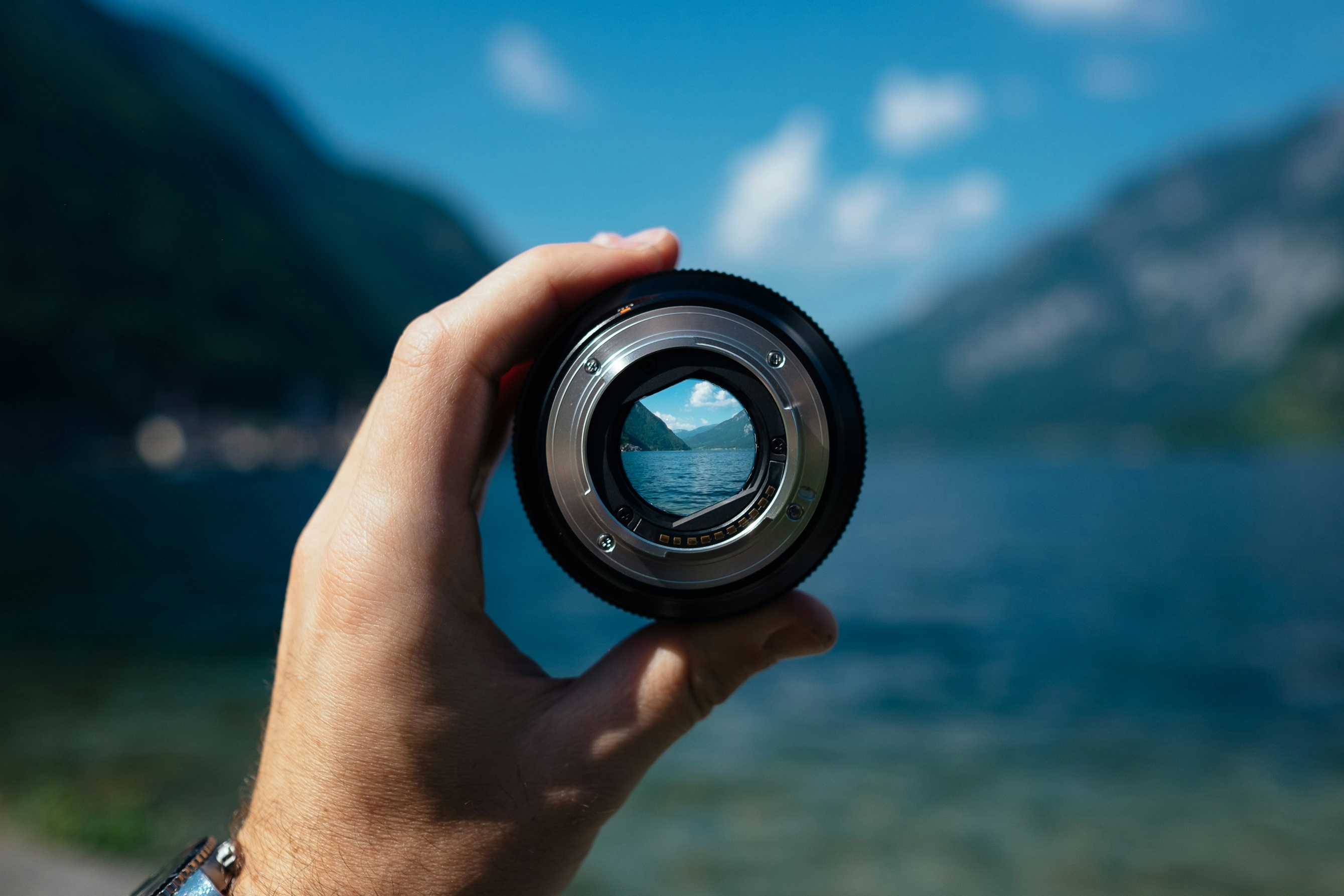 hand holding a camera lens where the area in the lens is in focus and the rest is blurry. Scene is of water on the horizon.